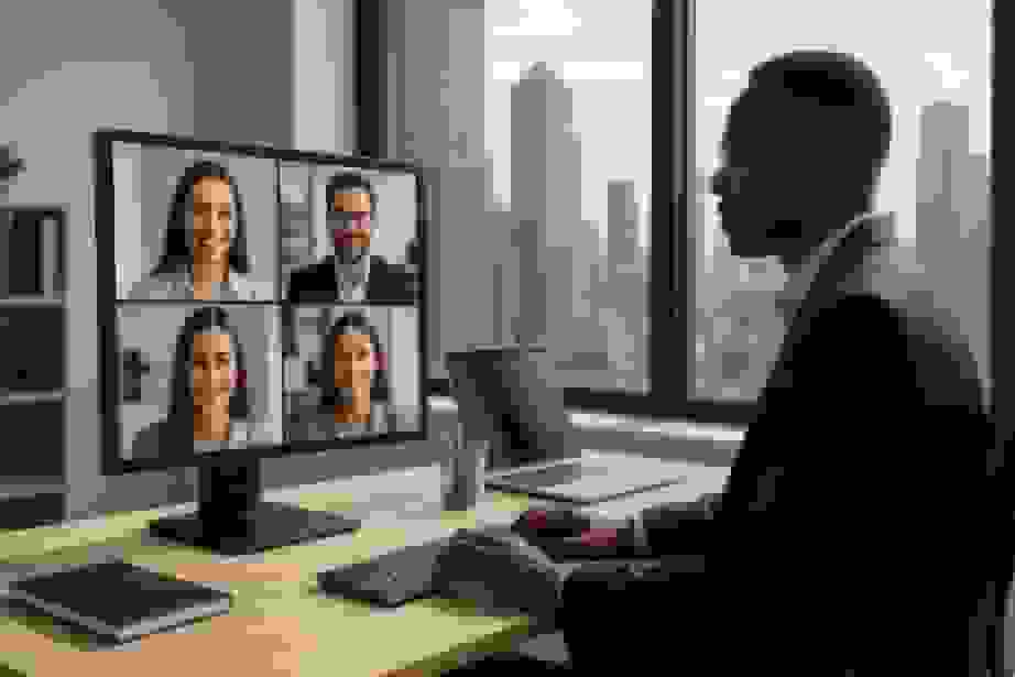 A man on a video call with four colleagues shown on the monitor