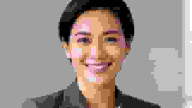 A close-up of a smiling professional Asian woman with short dark hair in a grey blazer.