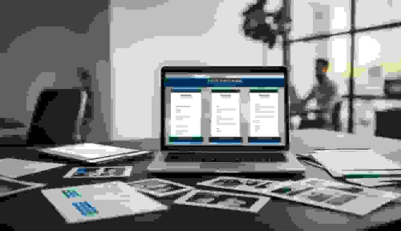 A laptop, a camera and printed photographs laid out on a desk