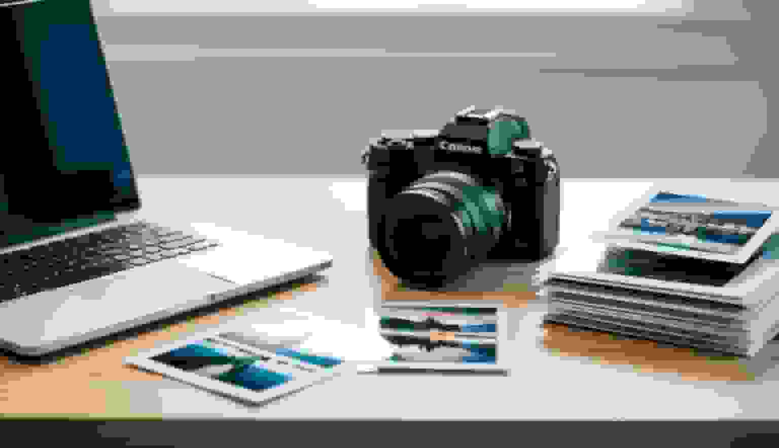 A laptop, a camera and printed photographs laid out on a desk
