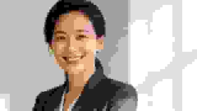 A confident and smiling Asian businesswoman in a suit looks directly at the camera.