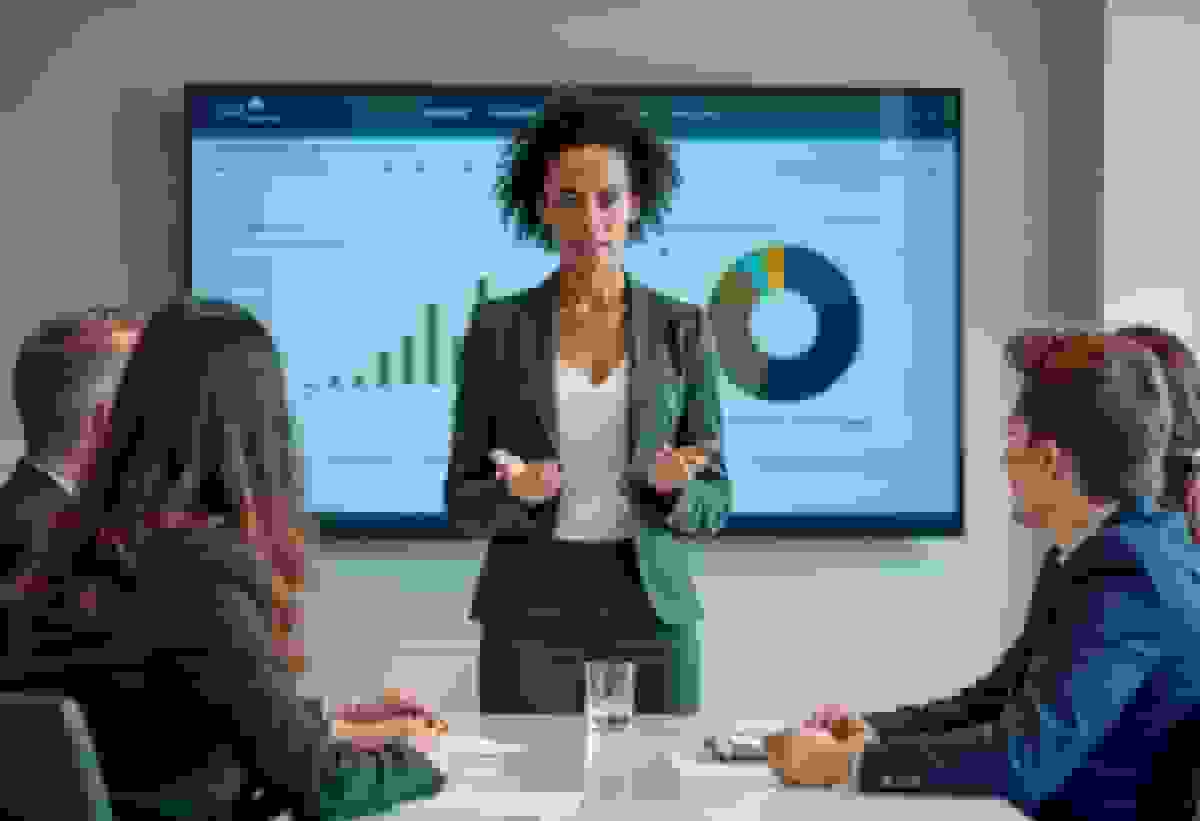 A woman presenting charts on a screen to colleagues around a meeting table