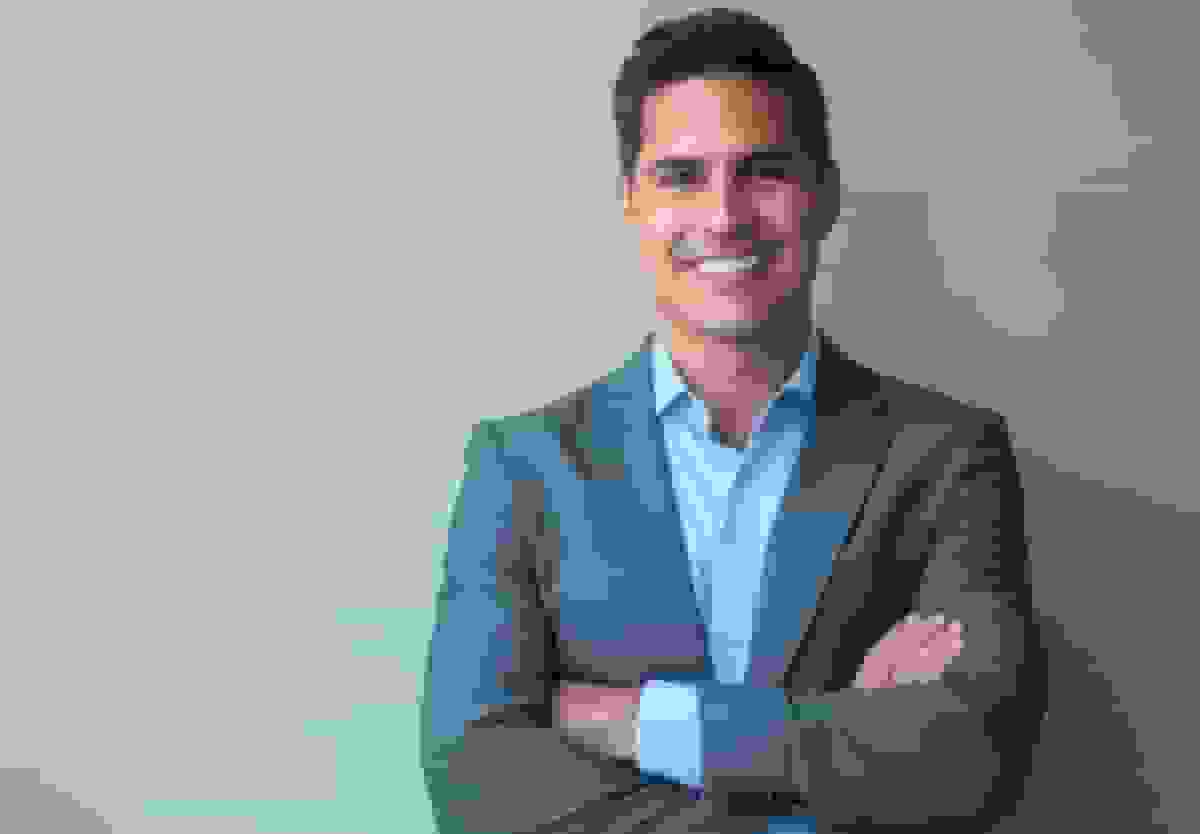 A man in business dress photographed against a plain studio backdrop