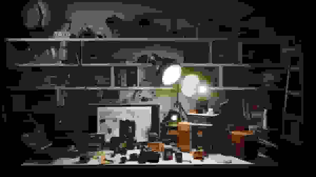 A studio shelf of vintage cameras and lighting equipment lit by a single lamp