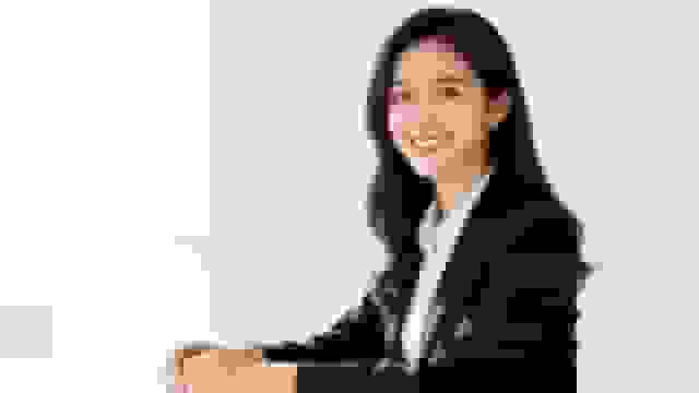 Smiling young Asian businesswoman in a black suit sitting at a table, looking at camera.