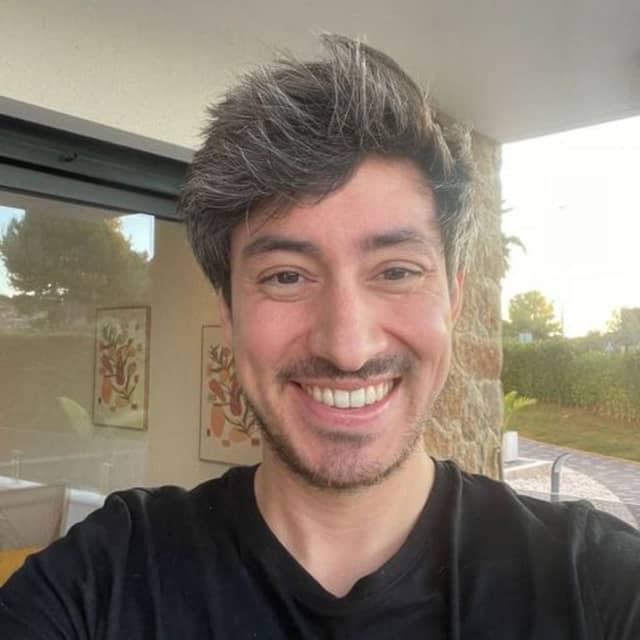 Input selfie, a man with thick greying hair and a beard in a black t-shirt, smiling in a bright living room