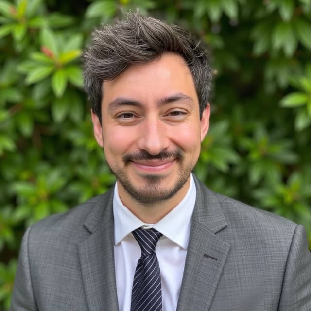 Man in a grey suit by a green hedge, with his beard and full cheeks retained