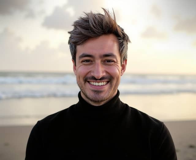 Man smiling on a beach at sunset, with recognisable grey hair and teeth