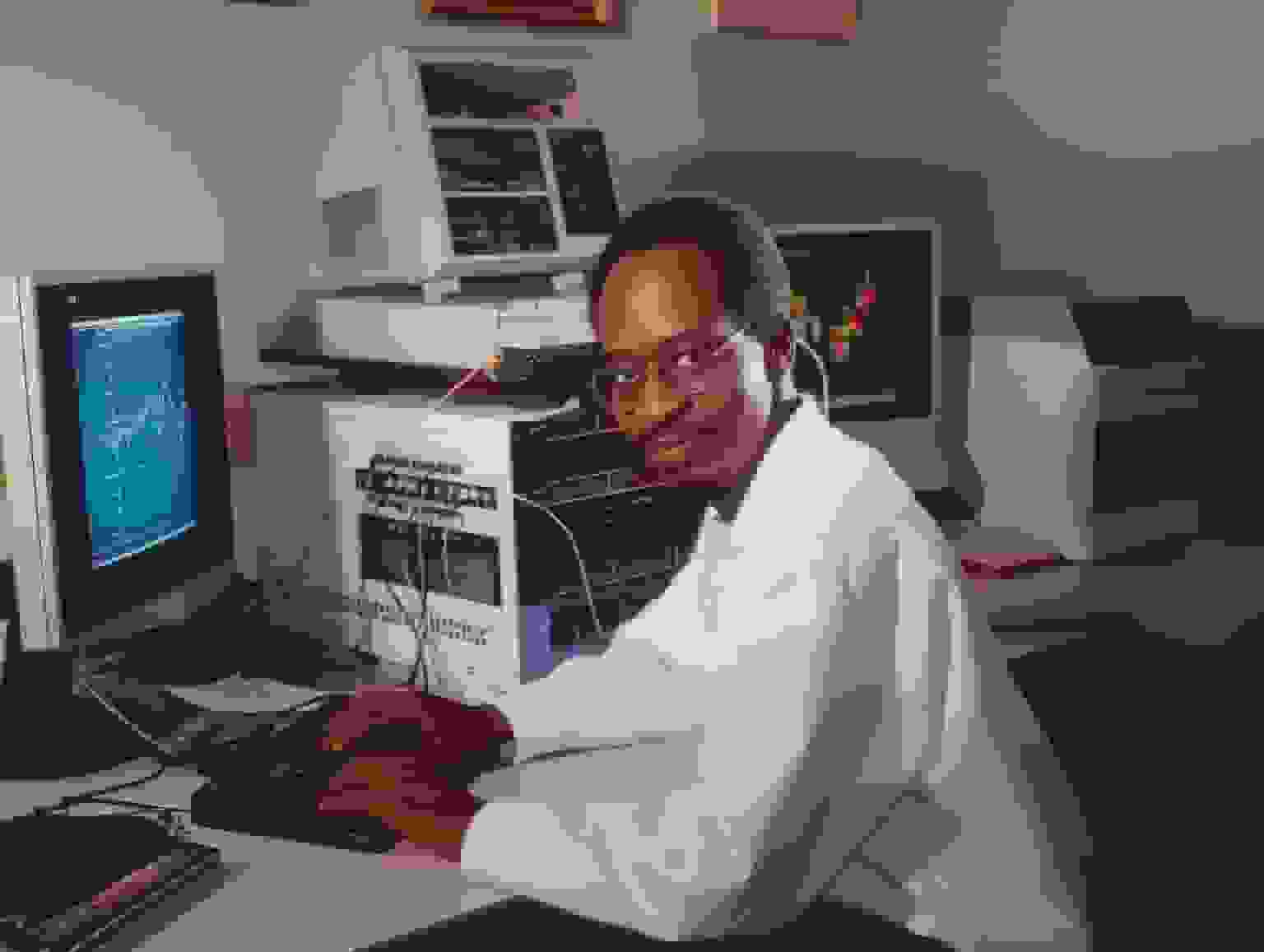 A man in a white lab coat working at a computer workstation
