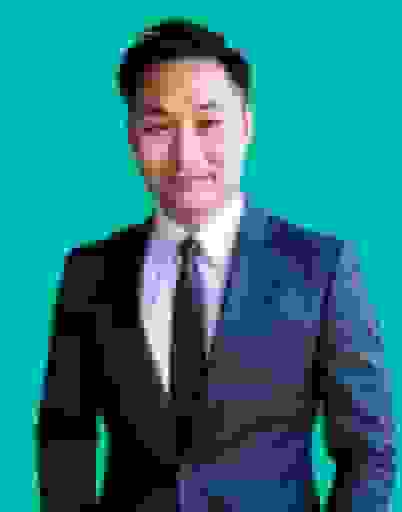 A man in a navy suit and dark tie against a teal background