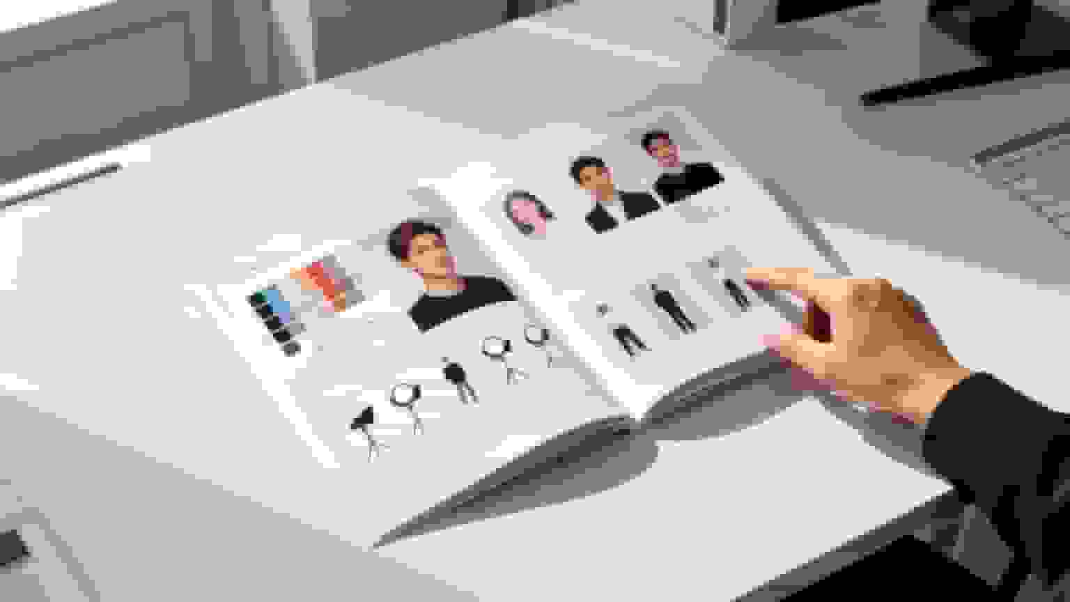 A hand points to an open photography style guide on a desk, displaying headshots and lighting examples.