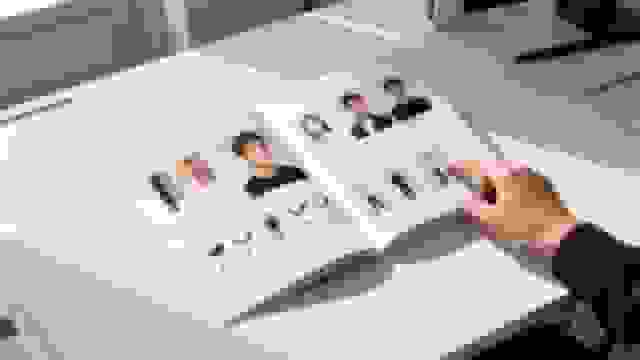 A hand points to an open photography style guide on a desk, displaying headshots and lighting examples.