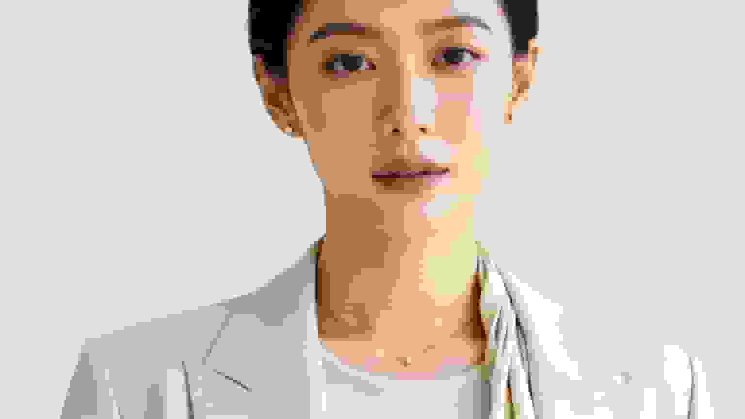 Close-up of an Asian woman in a light blazer, wearing pearl earrings and a necklace.