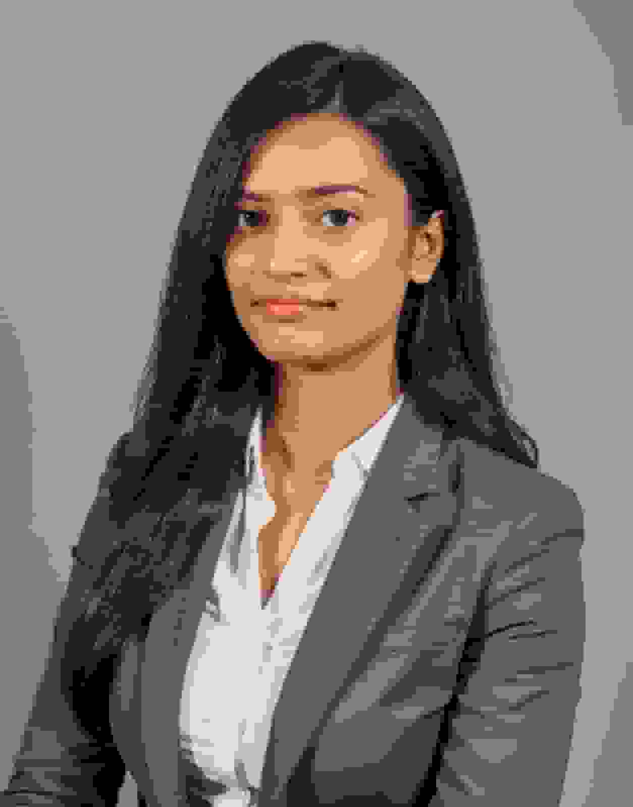 Headshot of a woman with long straight black hair worn down with a side part, in a grey blazer against a grey backdrop