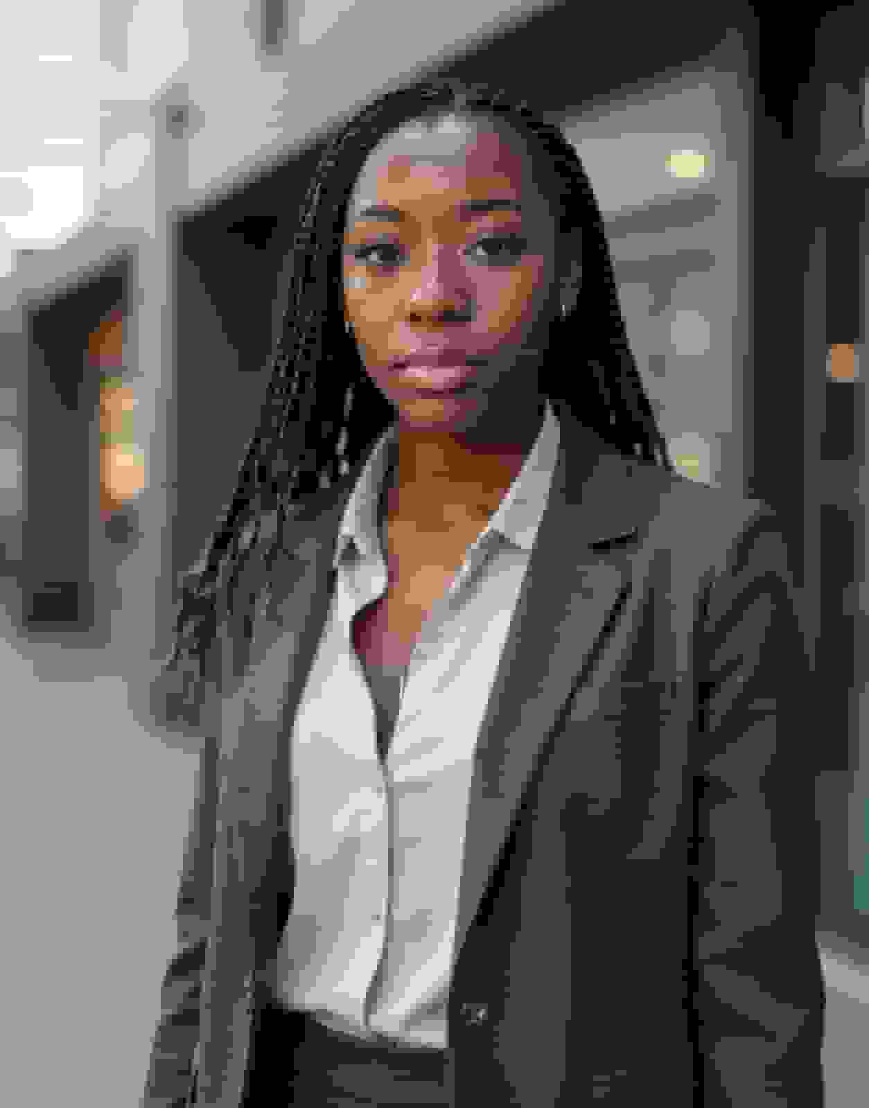 AI headshot of the same woman, with the same long braids and copper highlights, in a charcoal blazer on a blurred street
