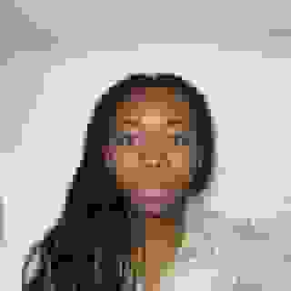 Phone selfie of a woman with long braids with copper highlights, against a white wall